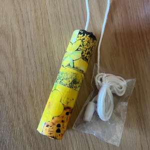 May include: A yellow floral light pull with a white cord and toggle. The cylindrical light pull features a design of yellow flowers and green leaves. The cord is looped and attached to the light pull. The toggle is white.