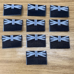 May include: Ten black fabric patches with a white Union Jack design. The patches are rectangular and have a slightly textured surface.
