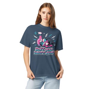 Pode incluir: Camiseta azul marinho com um design gráfico. O design apresenta um borrifador rosa, formas geométricas e o texto "DON'T YOU SWEAT IT, BABY". Acabamentos de raios também estão incluídos.