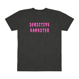 May include: A dark grey short-sleeve t-shirt featuring an all-over black leopard print pattern. The centre of the chest displays the text SENSITIVE GANGSTER in a bright pink, dripping, liquid-style font that stands out against the dark background.