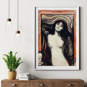May include: Framed art print of a woman with long black hair, a white dress, and a skeletal figure in the corner. The artwork has a white frame and is displayed on a wooden cabinet. Two pendant lights hang above.