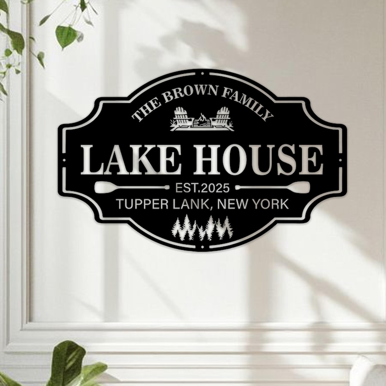 以下が含まれることがあります： 白い文字が入った黒い金属製のレイクハウスサイン。「The Brown Family Lake House Est. 2025 Tupper LANK, New York」と書かれています。2つの椅子とキャンプファイヤーのある湖のシーンが含まれています。
