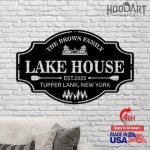以下が含まれることがあります： 黒い金属製のレイクハウスの看板。白で「The Brown Family」と「Lake House」の文字が入っています。「EST.2025」と「Tupper LANK, New York」の文字も含まれています。アディロンダックチェア、キャンプファイヤー、木のデザインが特徴です。