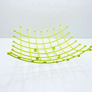 Pu&ograve; includere: Un cestino di frutta in metallo verde lime con un design a griglia. Il cestino ha una forma curva con estremit&agrave; arrotondate e piccoli accenti a sfera. La griglia &egrave; composta da linee sottili e dritte.