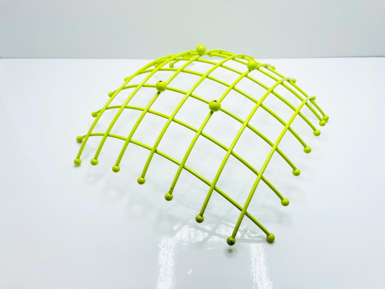 Pu&ograve; includere: Un cestino di frutta in metallo verde lime a forma di cupola. Il cestino ha un design a griglia con piccoli accenti rotondi alle intersezioni della griglia. Il cestino &egrave; su una superficie bianca.