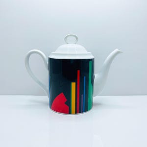 May include: White ceramic teapot with a black, red, yellow, green and blue geometric design.