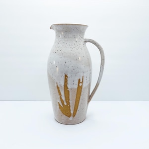 May include: A white ceramic jug with a speckled glaze and a gold leaf design. The jug has a wide mouth and a handle.
