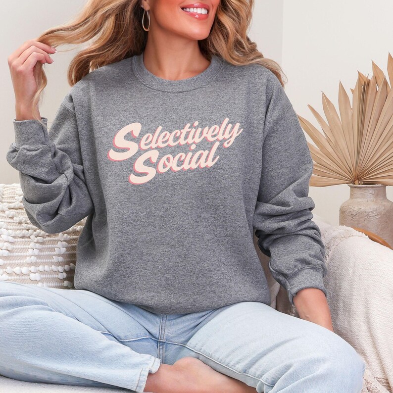 Woman sitting in a gray sweatshirt with the words "Selectively Social" written in a light pink script.