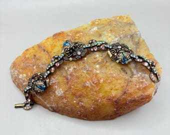 May include: A vintage bracelet with a floral design featuring pastel blue, pink, and green rhinestones. The bracelet is made of gold-toned metal and has a delicate chain.