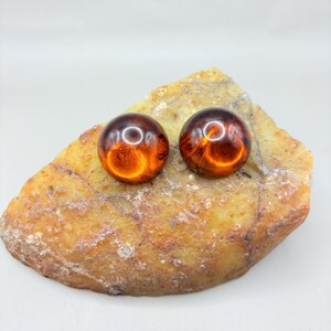 May include: A pair of round, amber-coloured earrings. The earrings are made of a translucent material with a slight shimmer.