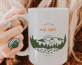 May include: White ceramic mug with a green mountain scene and the text "I lift up my eyes" in orange and brown. The text "Psalm 121" is printed in brown at the bottom of the mug.