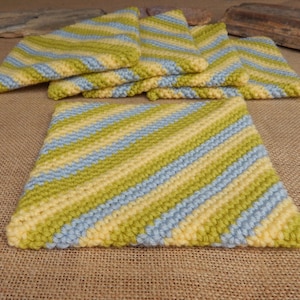 May include: A collection of handmade crochet items in shades of yellow, light blue, and green. The set includes square and triangular pieces, all with a striped pattern. The items appear to be kitchen or home decor.