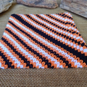May include: A crocheted dishcloth in orange, white, and black with a diagonal striped pattern.