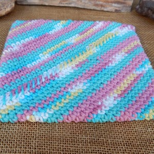May include: A square knitted dishcloth in a diagonal striped pattern of pink, blue, white, and yellow.