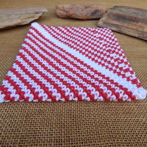 May include: A red and white crocheted dishcloth with a diagonal pattern. The dishcloth is made with a textured yarn and has a square shape.