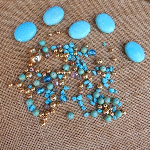 May include: A collection of turquoise and gold beads, including round, oval, and irregular shapes. The beads are scattered on a brown burlap background.