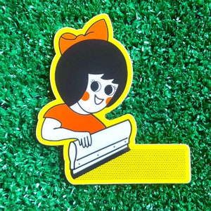 May include: A yellow and orange sticker featuring a cartoon girl with a red bow in her hair using a squeegee to apply a yellow sticker with a dotted pattern.