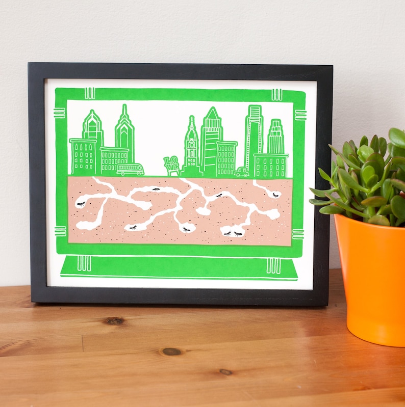 May include: A framed print of a city skyline with a green background and a brown ant colony underneath. The city skyline is made up of tall buildings with windows and a bus driving on the road. The ant colony is made up of brown dirt with white lines representing tunnels.