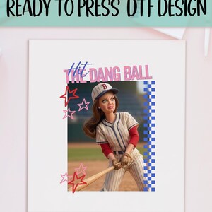 May include: A DTF design featuring a doll in a baseball uniform, holding a bat. The text "Hit Dang Ball" is above the doll, with star accents. The design is on a white background.