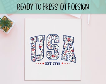 May include: White graphic featuring the word "USA" in a floral pattern with red and blue accents, and the text "EST. 1776". The design is suitable for DTF (Direct to Film) printing.