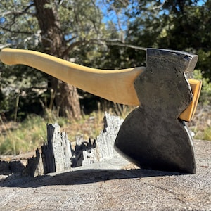 以下が含まれることがあります： 明るい木製の柄と濃い色の金属製の頭が付いた、ヴィンテージの斧。 斧頭は角度がついており、鋭い刃が付いています。 斧は風化した木製の表面に置かれており、自然な背景があります。