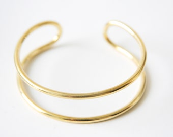 May include: A gold-toned double-band bangle bracelet. The bracelet is made of two smooth, rounded bands of metal.