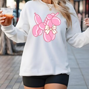 May include: White sweatshirt with a pink balloon animal unicorn graphic. The unicorn has a yellow bow.