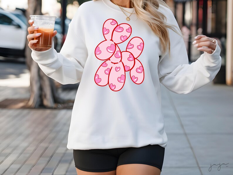 May include: White sweatshirt with a pink and red graphic of a balloon animal shaped like a dog with hearts on it.