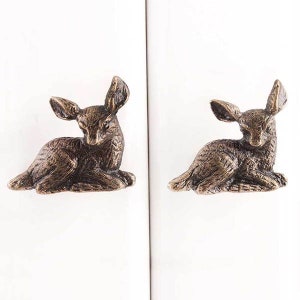 May include: Two antique bronze deer figurine cabinet knobs. The deer are lying down with their heads turned to the side.