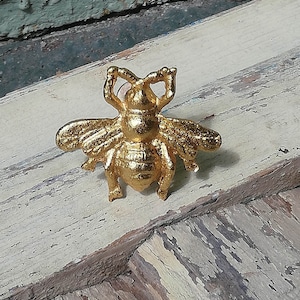 May include: A gold bee-shaped cabinet knob or drawer pull. The bee is detailed with textured wings and a raised body.