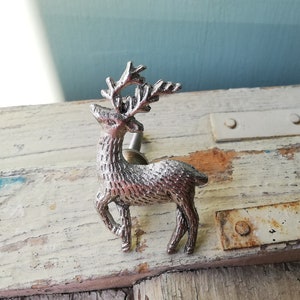 May include: Silver reindeer drawer pull with a detailed design. The reindeer is standing on all four legs with its head turned to the side. The antlers are curved and have a detailed design.