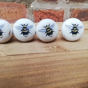 May include: Four white ceramic knobs with a bee design. Each knob features a black and yellow bee with wings and a white background.
