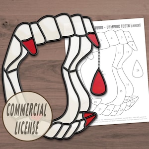 May include: A black and white stained glass pattern of a vampire hand with red nail polish and a red teardrop hanging from a chain. The pattern is labeled "Vampire Teeth (Large)" and includes numbered sections for coloring.