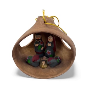May include: A handcrafted nativity scene inside a bell-shaped terracotta ornament. The scene features painted figurines of Mary, Joseph, baby Jesus, and animals. The ornament has a yellow string for hanging.