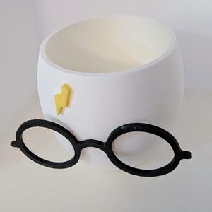 May include: White ceramic planter shaped like a head with a yellow lightning bolt and black round glasses.