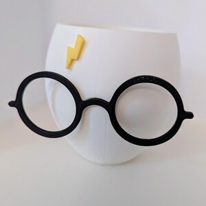 May include: White ceramic mug with a black lightning bolt decal and a pair of black round glasses attached to the side.