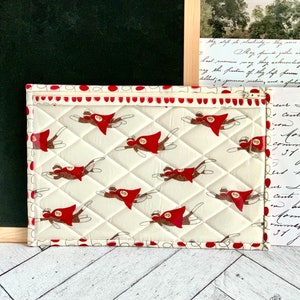 May include: A white quilted zippered pouch with a red and white polka dot trim. The pouch features a repeating pattern of monkeys wearing red capes and flying.