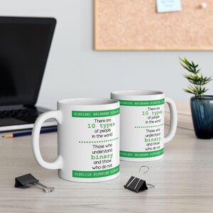 May include: Two white ceramic mugs with a green and white design. The mugs feature the text "There are 10 types of people in the world. Those who understand binary and those who do not." with binary code at the top and bottom of the text.