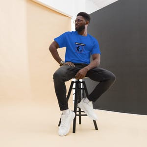 May include: A person wearing a blue t-shirt with the text "Service Human" and a graphic of a person walking a dog. The person is sitting on a black stool.