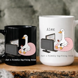 Könnte beinhalten: Zwei Keramikbecher, einer schwarz und einer weiß, mit einem Cartoon-Gans-Design. Die Gans sitzt auf einem rosa Kissen vor einem Computer. Der Text "Just a Friendly Bug-Fixing Goose" ist auf beiden Bechern aufgedruckt. Auf dem weißen Becher steht der Name "Alex".