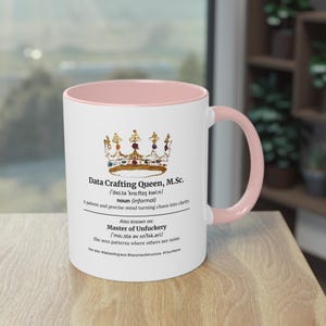 Op de afbeelding: Witte keramische mok met een roze binnenkant en handvat. De mok heeft de tekst "Data Crafting Queen, M.Sc." met een kroonillustratie en extra tekst. De mok is ontworpen voor dranken.