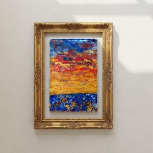 Peut inclure: Une peinture abstraite d'un coucher de soleil dans un cadre doré orné. L'œuvre présente un ciel vibrant aux teintes bleues, rouges et jaunes. La partie inférieure de la peinture a une base bleue avec des accents jaunes. Le cadre est de couleur or chaud.