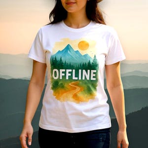 Könnte beinhalten: Weißes T-Shirt mit einem Aquarell-Landschaftsmotiv, das einen Berg, Bäume und eine Sonne zeigt. Das Wort "OFFLINE" ist in Weiß gedruckt. Das Shirt ist aus weichem Material und hat kurze Ärmel.