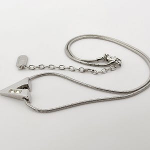 May include: A silver necklace with a triangular pendant featuring two clear rhinestones. The necklace has a snake chain and a lobster clasp.