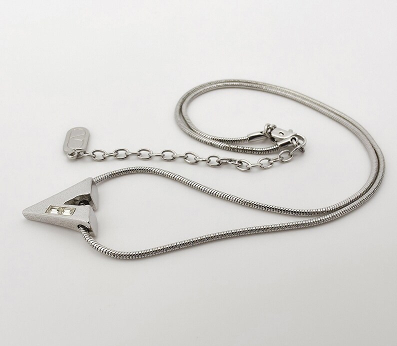 May include: A silver necklace with a triangular pendant featuring two clear rhinestones. The necklace has a snake chain and a lobster clasp.