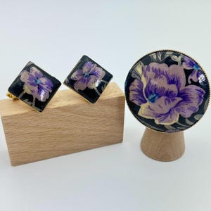 ヴィンテージの花柄スクリュークリップイヤリングとそれにマッチするブローチペンダントコンボ。黒地に紫の花が描かれ、ゴールドのトリムアクセントがアクセントになっています。