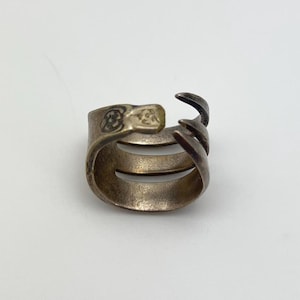 May include: Silver ring with a claw design. The ring is made of two bands of metal that are twisted together. The claw is made of a single band of metal that is bent into a claw shape.