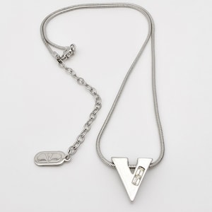 May include: A silver chain necklace with a silver pendant shaped like the letter V. The pendant has a small clear crystal in the center.