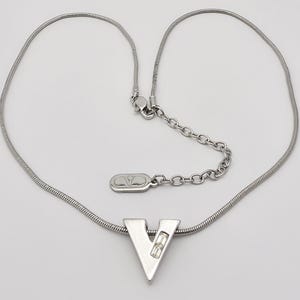 May include: A silver chain necklace with a silver pendant in the shape of the letter V. The pendant has a small clear stone in the center.