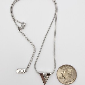 May include: A silver chain necklace with a silver pendant shaped like the letter V. The pendant has two small clear stones. The necklace is about 18 inches long.